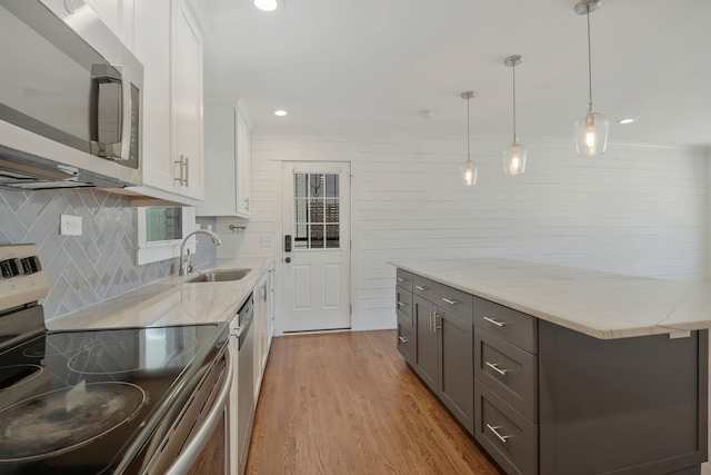 kitchen with white cabinets, appliances with stainless steel finishes, light wood-type flooring, pendant lighting, and sink