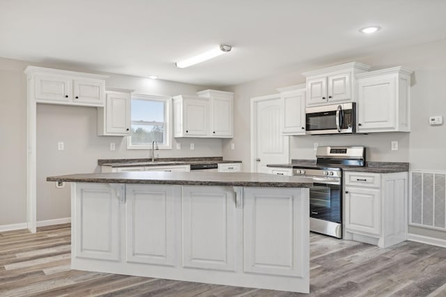 kitchen featuring appliances with stainless steel finishes, sink, light hardwood / wood-style flooring, white cabinets, and a center island