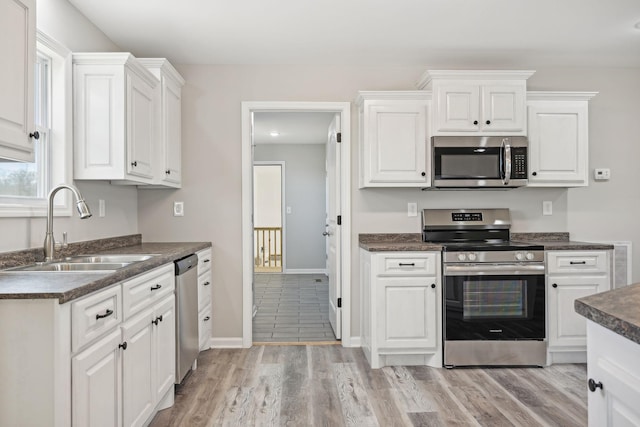 kitchen with white cabinets, appliances with stainless steel finishes, light hardwood / wood-style flooring, and sink