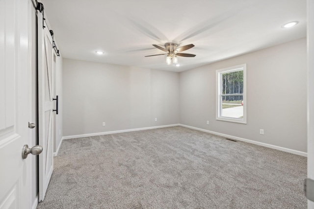 spare room with ceiling fan, a barn door, and light carpet