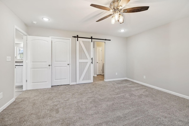 unfurnished bedroom featuring a barn door, light colored carpet, and ceiling fan