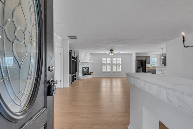 living room with light wood-type flooring, ceiling fan, and a brick fireplace