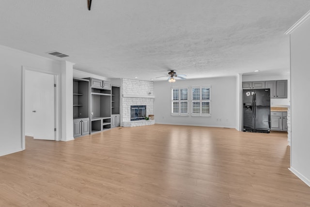 unfurnished living room with light hardwood / wood-style floors, ceiling fan, a textured ceiling, a fireplace, and crown molding