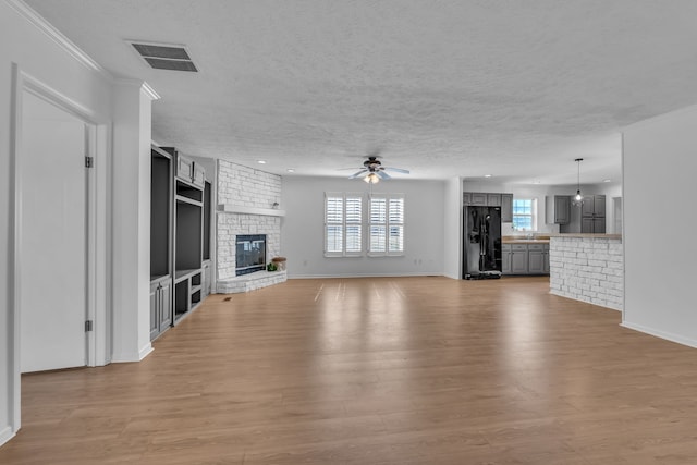 unfurnished living room featuring a brick fireplace, light wood-type flooring, a healthy amount of sunlight, and ceiling fan