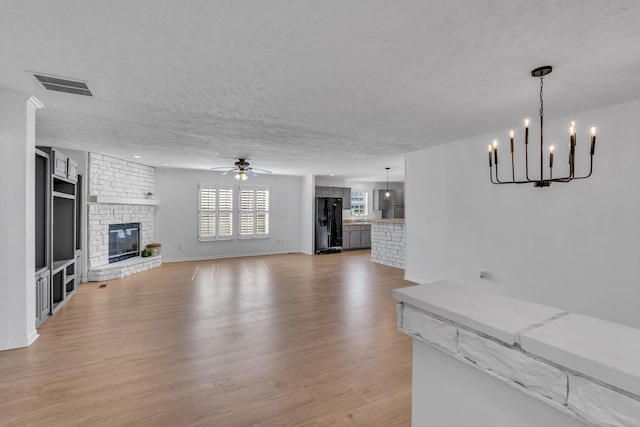 unfurnished living room featuring light wood-type flooring, a large fireplace, a textured ceiling, and ceiling fan with notable chandelier