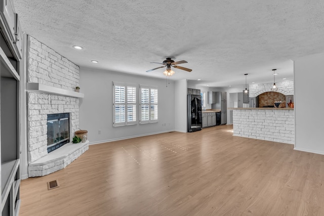 unfurnished living room with ceiling fan, a textured ceiling, light hardwood / wood-style floors, and a fireplace