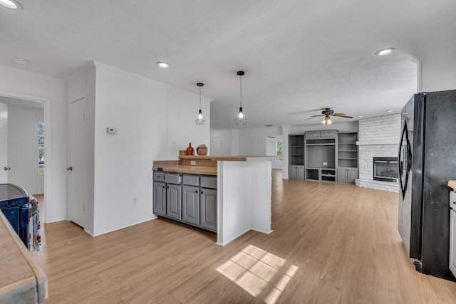 kitchen with light hardwood / wood-style flooring, black fridge, ceiling fan, and a brick fireplace