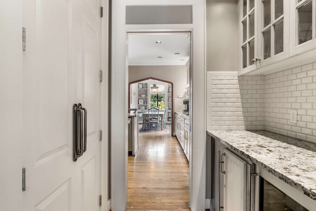 interior space featuring light stone counters, light hardwood / wood-style flooring, crown molding, and decorative backsplash