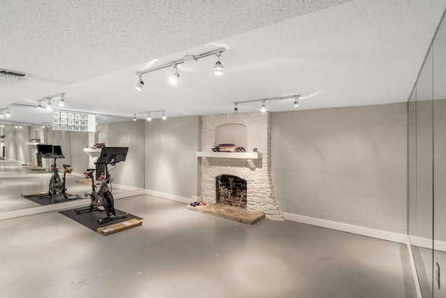 exercise area with a textured ceiling, a fireplace, concrete floors, and rail lighting