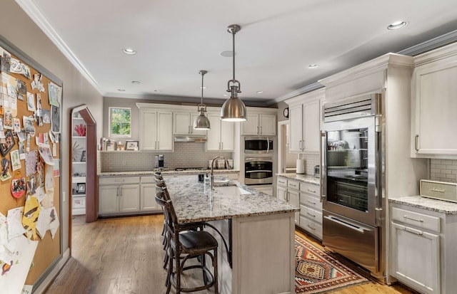 kitchen with sink, a kitchen island with sink, decorative light fixtures, light hardwood / wood-style flooring, and light stone countertops