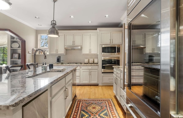 kitchen with built in appliances, pendant lighting, light hardwood / wood-style flooring, a center island with sink, and sink