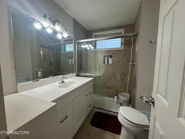 bathroom with tile patterned flooring, a shower with door, vanity, and toilet