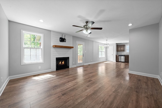 unfurnished living room featuring ceiling fan with notable chandelier, dark hardwood / wood-style floors, and a large fireplace