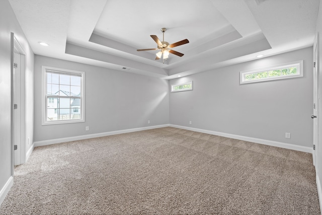 carpeted empty room with a tray ceiling, ceiling fan, and a wealth of natural light