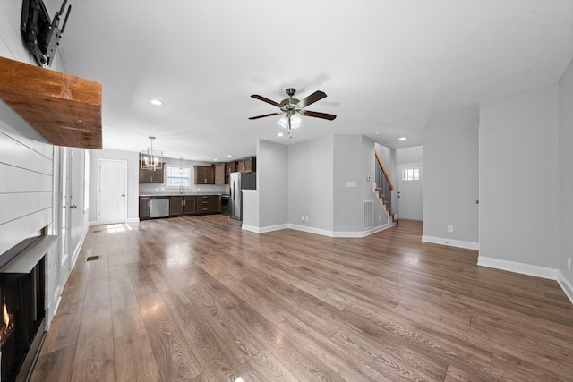 unfurnished living room with ceiling fan with notable chandelier and hardwood / wood-style floors