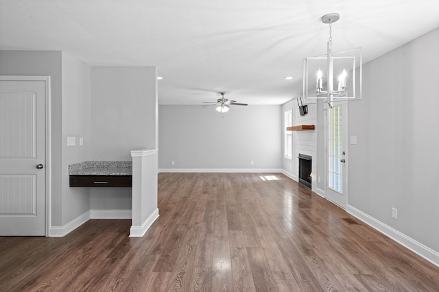 unfurnished living room featuring ceiling fan with notable chandelier, a large fireplace, and dark wood-type flooring