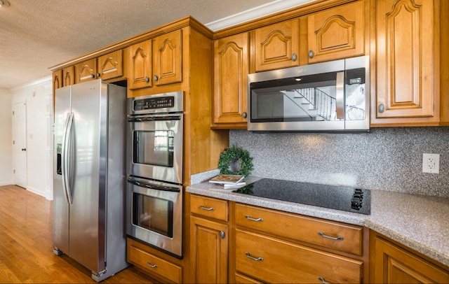 kitchen featuring appliances with stainless steel finishes, crown molding, light hardwood / wood-style floors, and tasteful backsplash