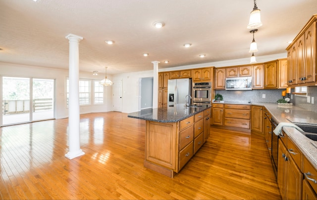 kitchen with appliances with stainless steel finishes, light hardwood / wood-style flooring, decorative light fixtures, decorative columns, and a kitchen island with sink