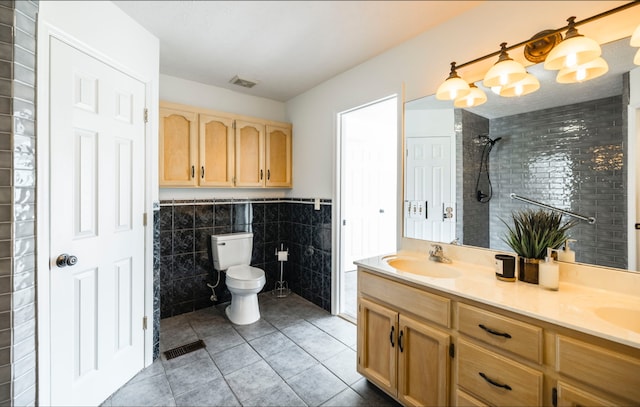 bathroom featuring vanity, toilet, tiled shower, tile walls, and tile patterned flooring