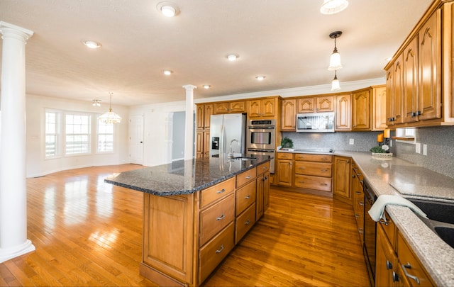 kitchen featuring tasteful backsplash, stainless steel appliances, decorative columns, a kitchen island with sink, and hardwood / wood-style floors