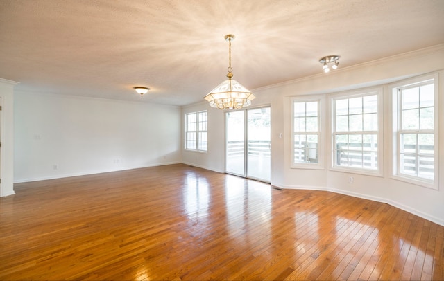 unfurnished room featuring a notable chandelier, ornamental molding, hardwood / wood-style floors, and a healthy amount of sunlight