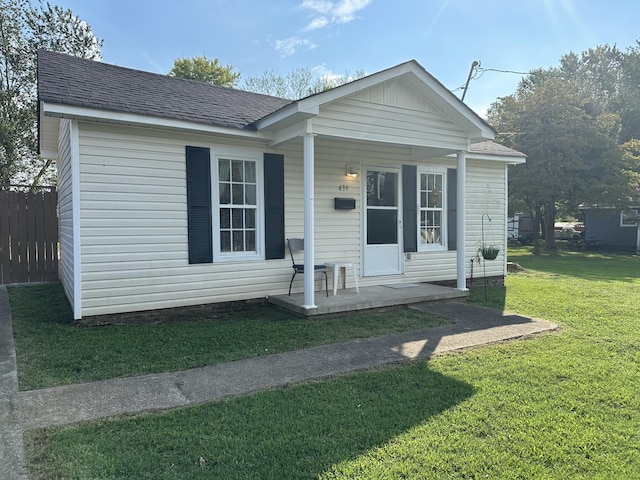 view of front facade with a porch, a front yard, a shingled roof, and fence