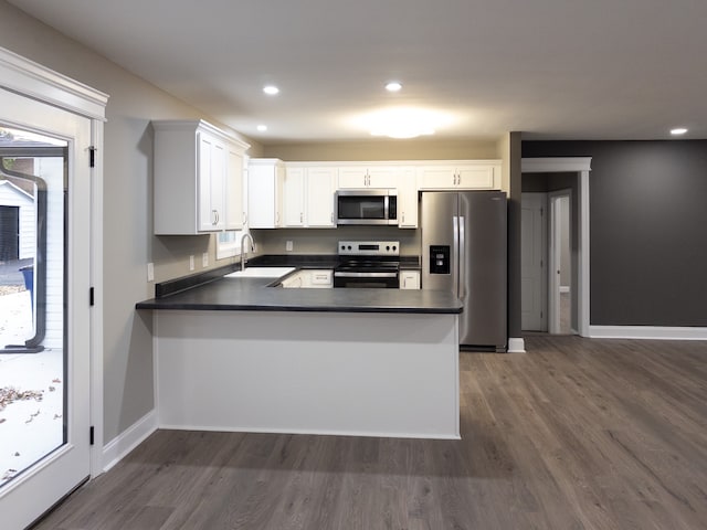 kitchen with sink, kitchen peninsula, white cabinetry, stainless steel appliances, and dark hardwood / wood-style flooring