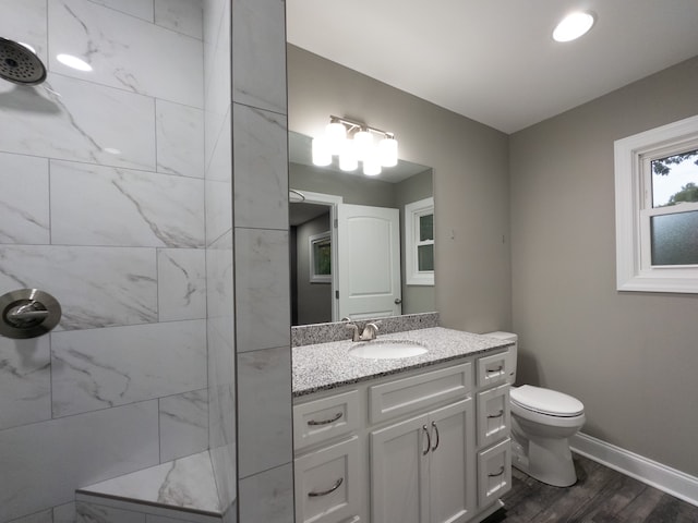 bathroom featuring hardwood / wood-style floors, vanity, tiled shower, and toilet