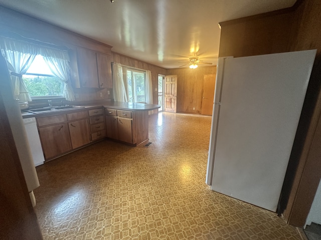 kitchen with white refrigerator, plenty of natural light, kitchen peninsula, and sink