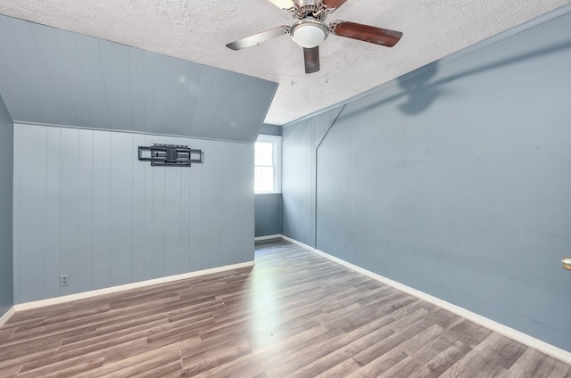 additional living space featuring a textured ceiling, wood-type flooring, vaulted ceiling, and ceiling fan