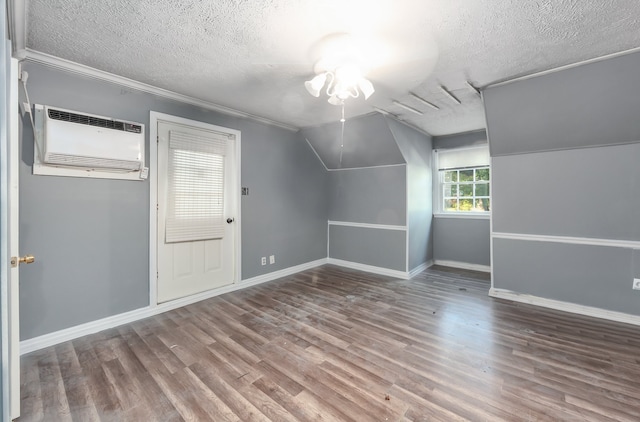 additional living space featuring a wall unit AC, a textured ceiling, vaulted ceiling, hardwood / wood-style floors, and ceiling fan