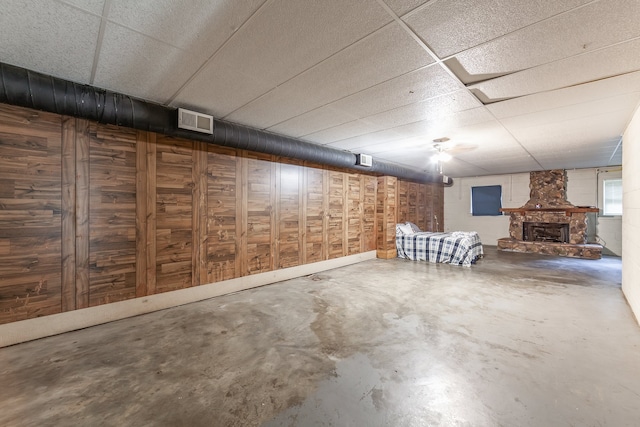 basement featuring a drop ceiling, wood walls, and a fireplace