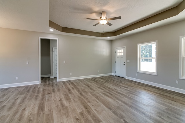 unfurnished room featuring light hardwood / wood-style floors, ceiling fan, a tray ceiling, and a textured ceiling