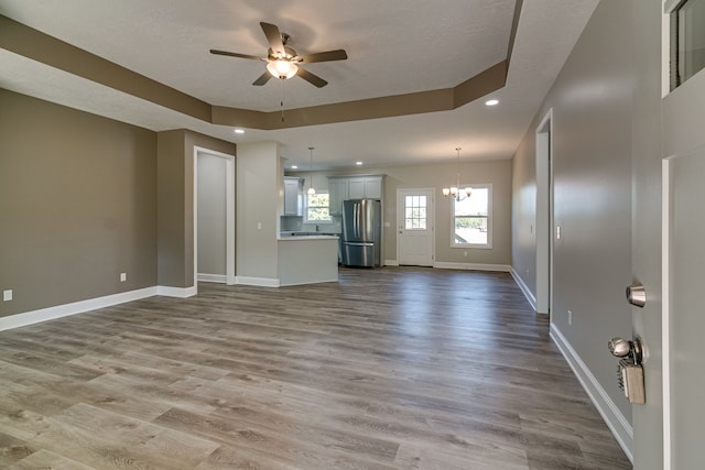 unfurnished living room with a textured ceiling, ceiling fan with notable chandelier, hardwood / wood-style floors, and a raised ceiling