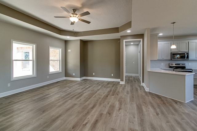 unfurnished living room featuring ceiling fan, a textured ceiling, light wood-type flooring, and a tray ceiling