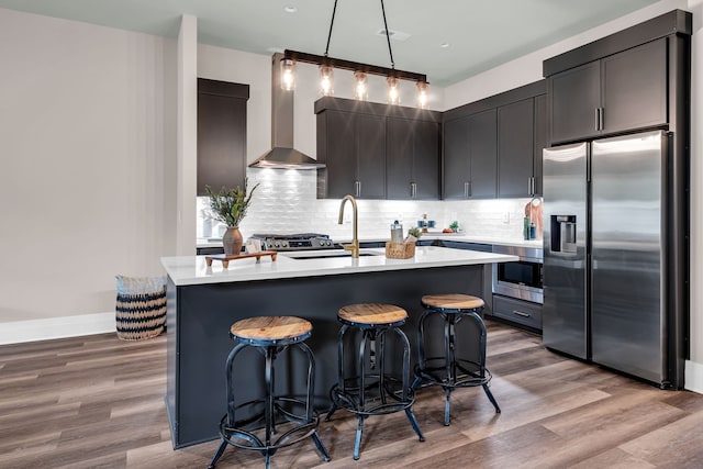 kitchen with appliances with stainless steel finishes, light hardwood / wood-style floors, wall chimney exhaust hood, pendant lighting, and sink