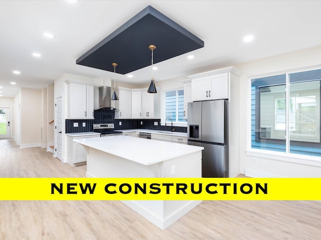 kitchen with hanging light fixtures, stainless steel appliances, wall chimney exhaust hood, and plenty of natural light