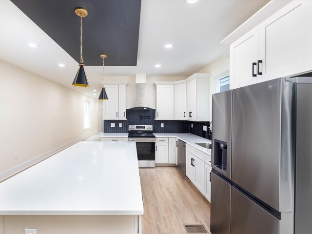 kitchen featuring white cabinets, hanging light fixtures, appliances with stainless steel finishes, light countertops, and wall chimney exhaust hood