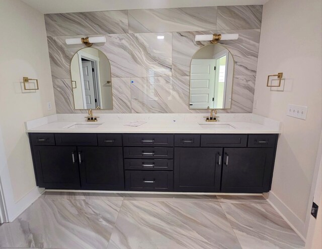 full bath featuring double vanity, marble finish floor, and a sink