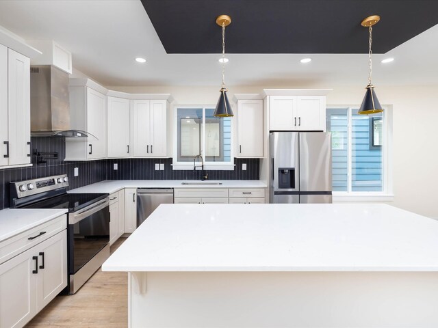 kitchen with hanging light fixtures, wall chimney exhaust hood, appliances with stainless steel finishes, and a sink