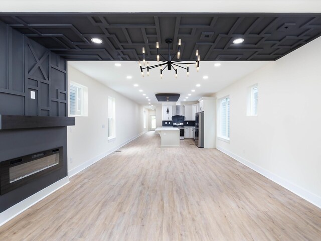 unfurnished living room featuring recessed lighting, a notable chandelier, a fireplace, baseboards, and light wood-style floors