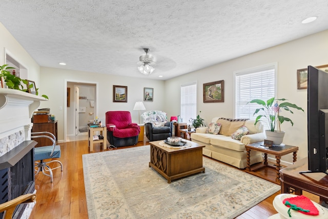 living room featuring ceiling fan, light wood-type flooring, and a textured ceiling