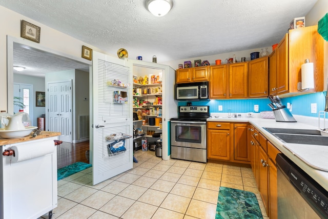 kitchen featuring light tile patterned floors, stainless steel appliances, sink, and a textured ceiling