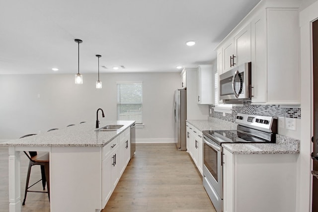 kitchen with white cabinets, hanging light fixtures, sink, a center island with sink, and stainless steel appliances