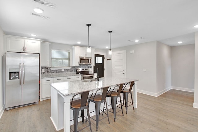 kitchen featuring appliances with stainless steel finishes, light stone counters, white cabinets, light hardwood / wood-style flooring, and a center island with sink