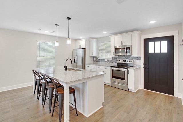 kitchen with appliances with stainless steel finishes, hanging light fixtures, light hardwood / wood-style floors, light stone counters, and white cabinets