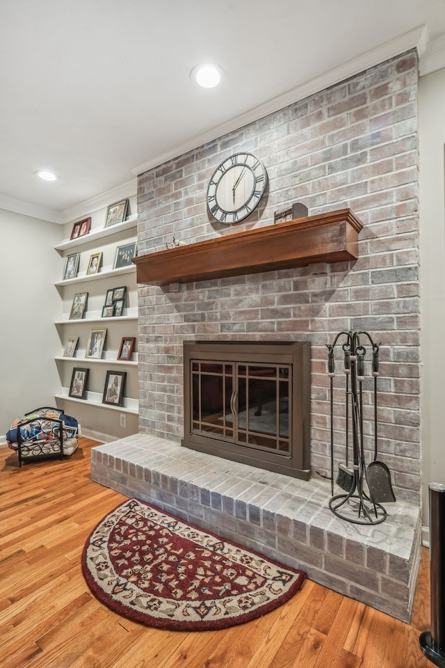 living room featuring a brick fireplace, ornamental molding, and wood-type flooring