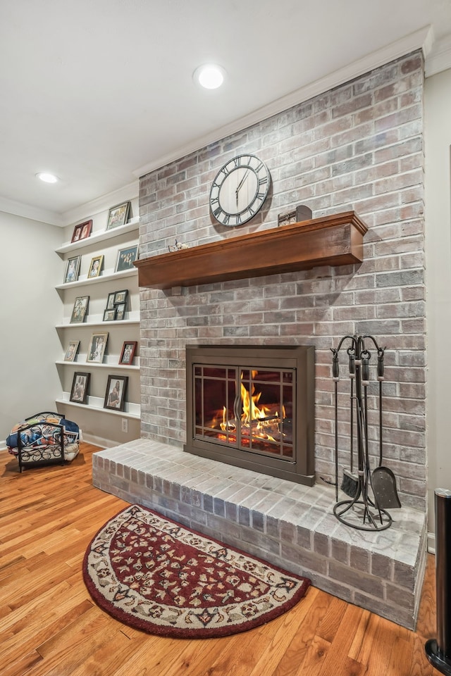 living room with a brick fireplace, crown molding, and hardwood / wood-style floors