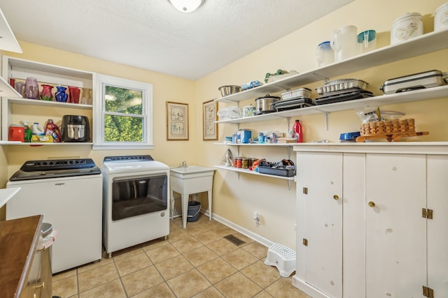 clothes washing area featuring a textured ceiling, light tile patterned floors, and washing machine and clothes dryer