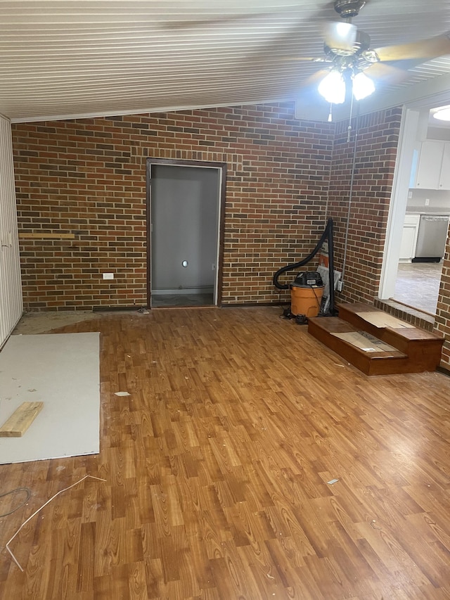 interior space with ceiling fan, light hardwood / wood-style floors, lofted ceiling, and brick wall